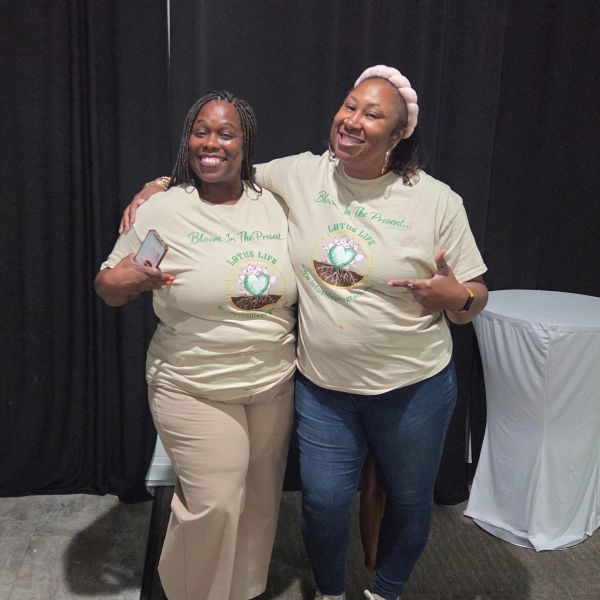 Two women smiling and pointing at matching shirts with a motivational message.