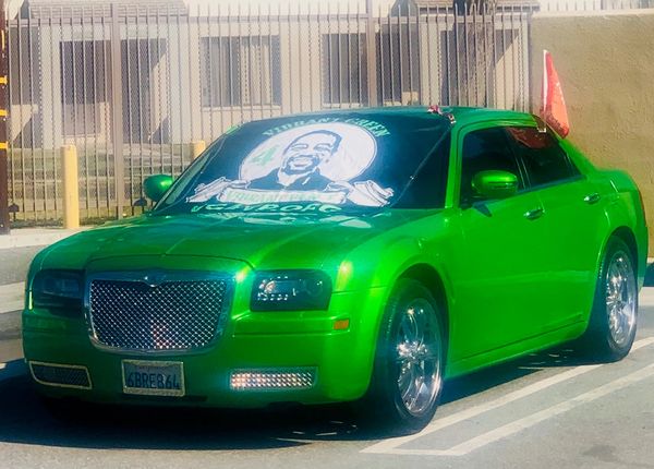A bright green Chrysler with a large graphic of a person on the windshield, parked in a lot.