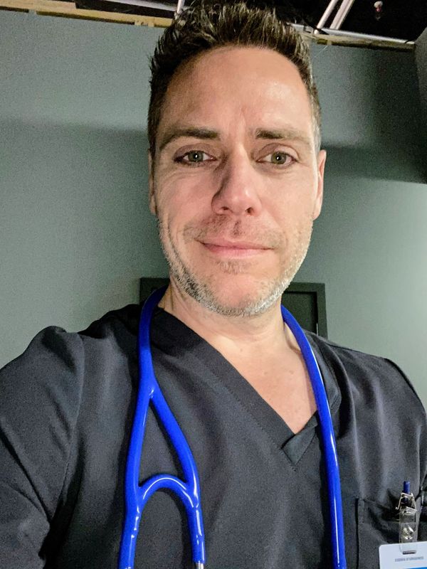 Smiling healthcare professional in black scrubs with blue stethoscope.