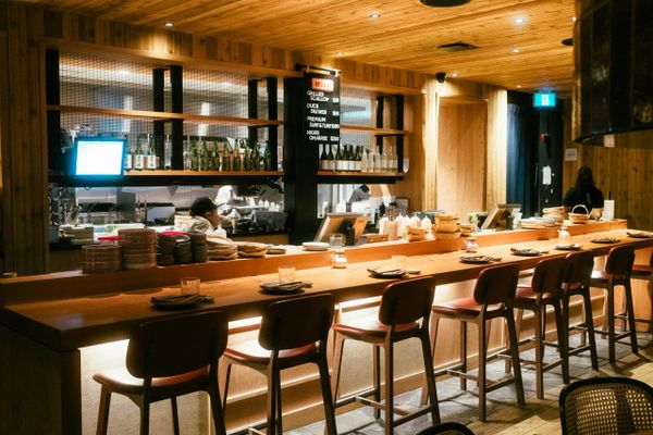 Cozy wooden bar with stools and neatly arranged plates in a warm-lit restaurant.