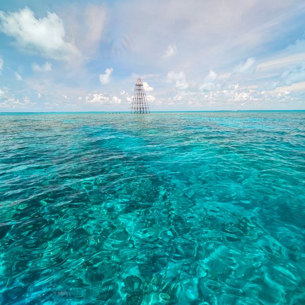 Clear turquoise ocean with a distant metal structure under a partly cloudy sky.