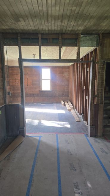 Room under renovation with exposed wooden framing and sunlight through a window.
