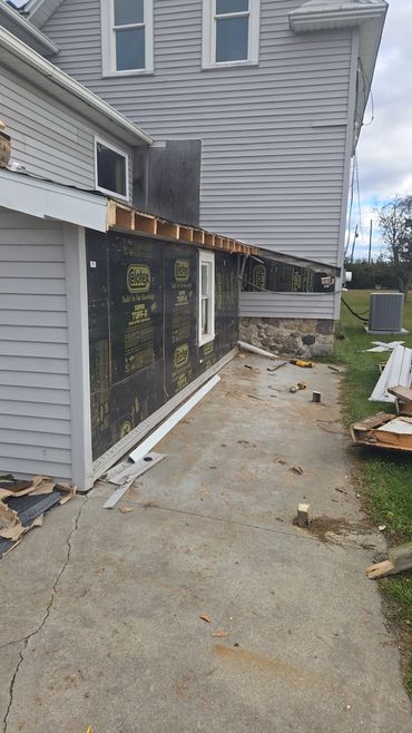 House siding renovation in progress with exposed insulation and construction debris.