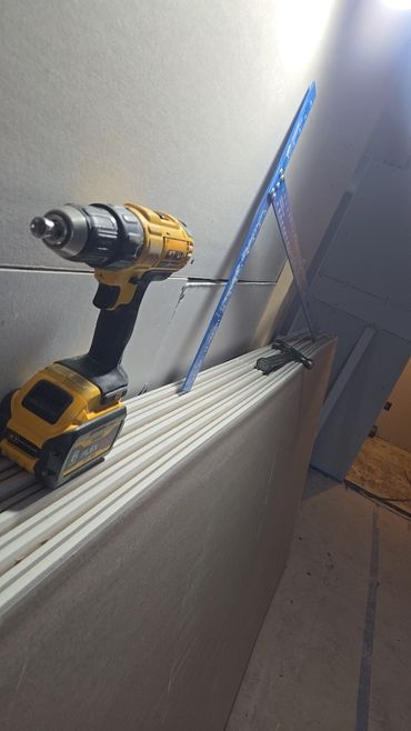 Power drill, square ruler, and hammer on drywall sheets in a construction setting.