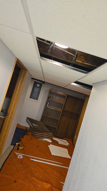Room under renovation with ceiling tiles and tools scattered on floor.