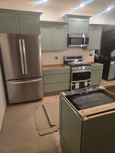 Modern kitchen installation in progress with sage green cabinets and stainless steel appliances.