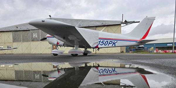 Small aircraft reflected in a puddle on an overcast day at an airport.