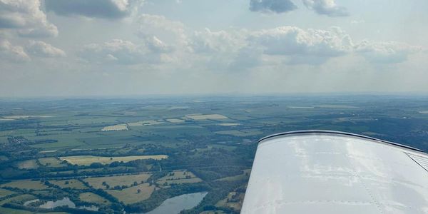 View from an airplane window showing a wing and countryside below under a partly cloudy sky.