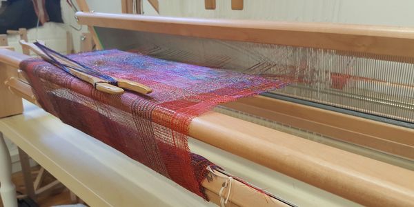 A colorful handloom weaving fabric with red and purple threads.