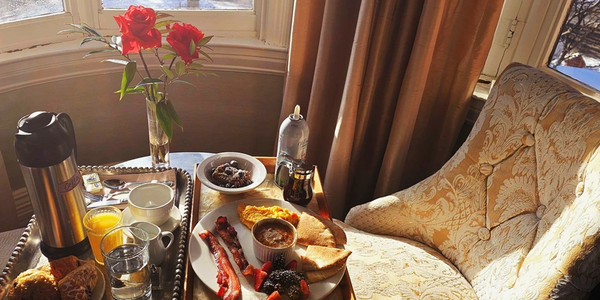 Cozy breakfast setup with flowers, orange juice, and a plate of eggs and bacon by a sunlit window.