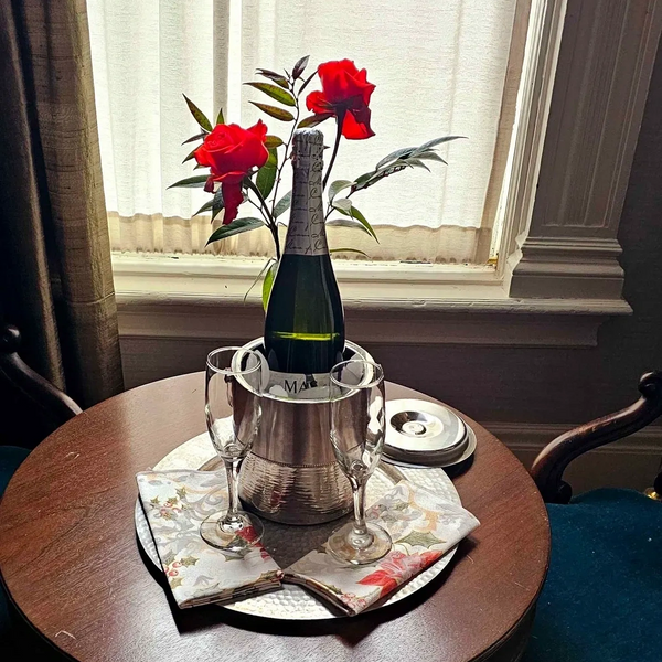 Champagne bottle with roses and glasses on a wooden table by a window.