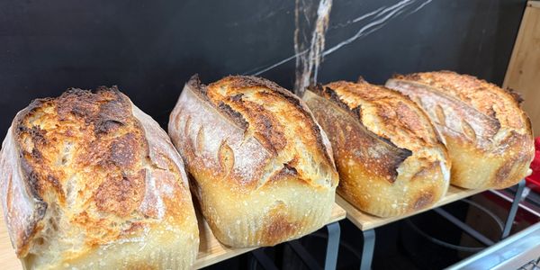 Four freshly baked golden crusted loaves of bread on wooden shelves.