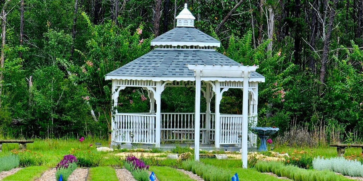 White gazebo amidst vibrant garden, colorful flowers & lush greenery. Tranquil outdoor haven.