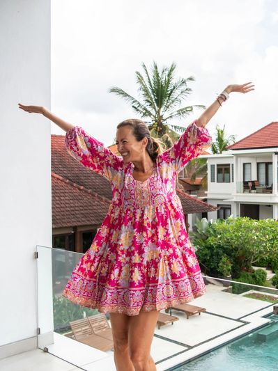 Happy woman in a colorful dress outside by a pool.