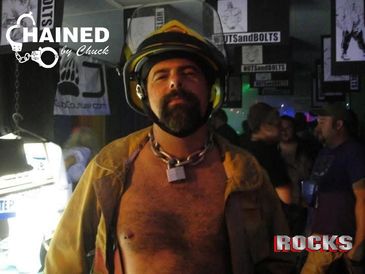 Man wearing firefighter helmet and jacket with a chain lock around his neck at a party.