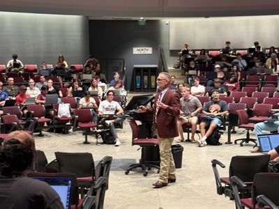 A professor lectures to attentive students in a large university classroom.