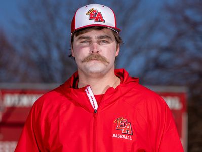 A man in a red EA Baseball jacket and cap with a mustache.