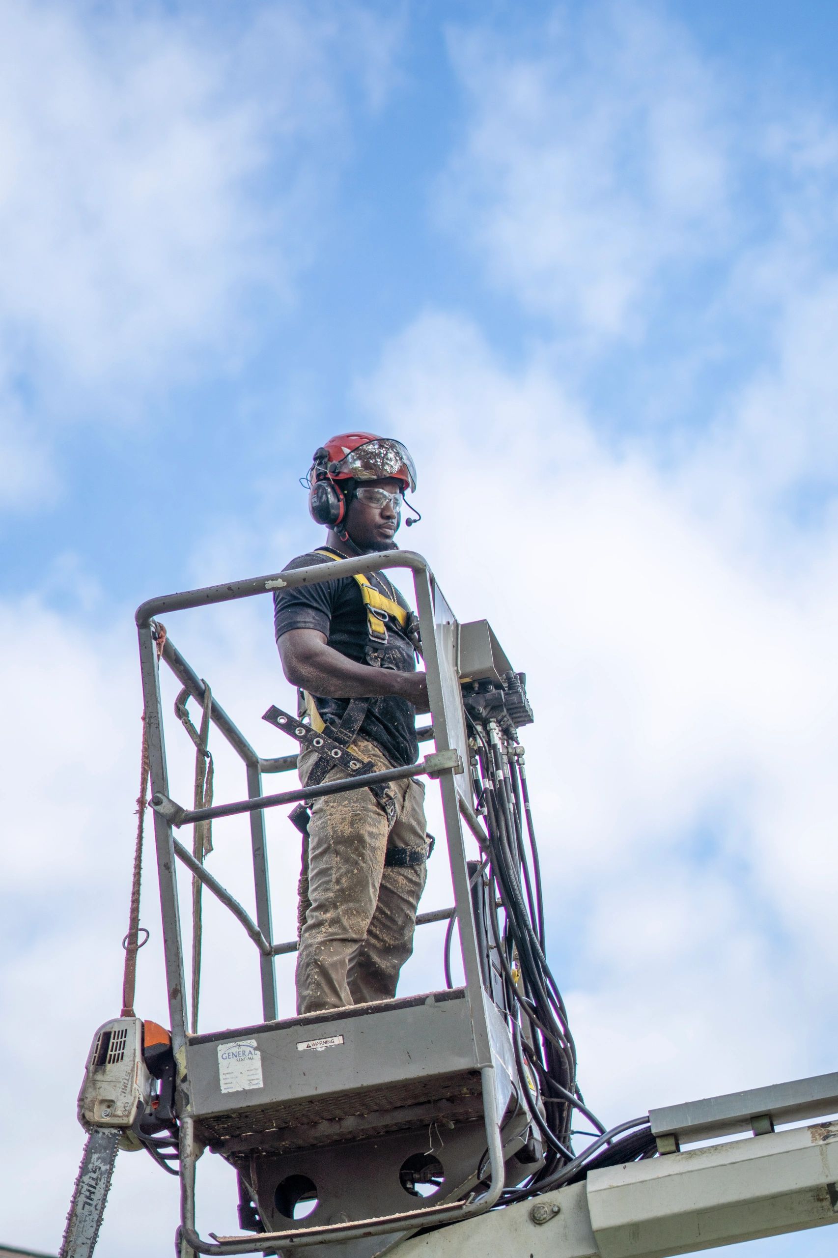 Worker in safety gear operating machinery high above ground under blue sky.