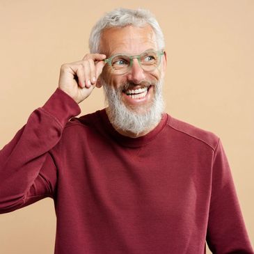 Smiling elderly man with white beard adjusting his green glasses.