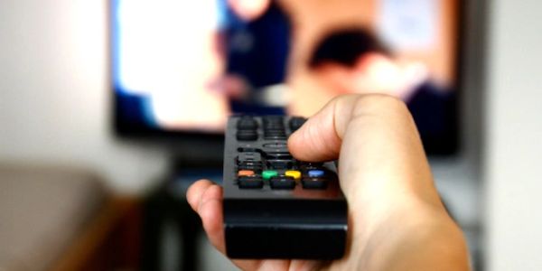 Hand holding a remote control pointing at a TV screen.