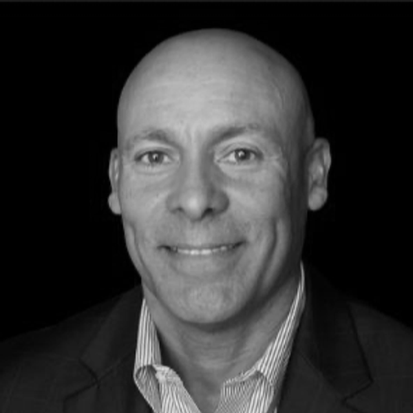 Black and white portrait of a smiling bald man in a suit jacket.