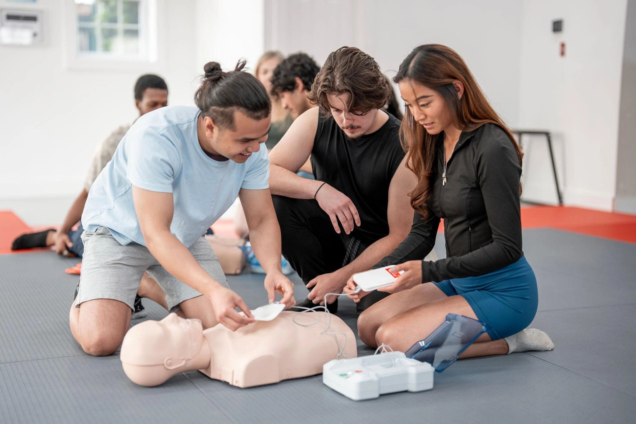 Group practicing CPR with a training manikin and AED device indoors.
