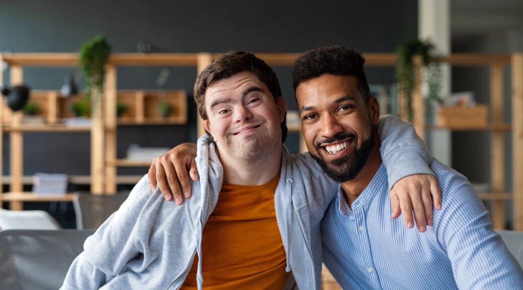 Two friends smiling warmly with arms around each other indoors.