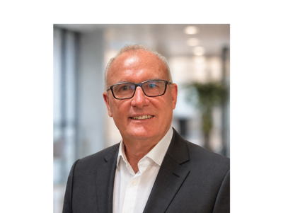 Smiling businessman in glasses wearing a dark suit and white shirt indoors.