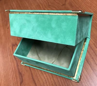 A luxurious, vintage-style box with teal suede covering, gold accents, and ornate metal corners
