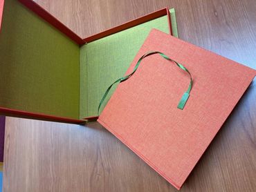 Handmade cloth-covered book box with green ribbon and fabric lining.