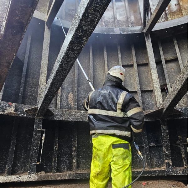 Worker power washing a large, industrial metal structure on commercial cleaning job