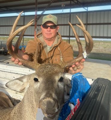 Man proudly holds large deer antlers in an outdoor covered area.