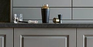 Modern kitchen with gray cabinetry, dark dining table, and green chairs.