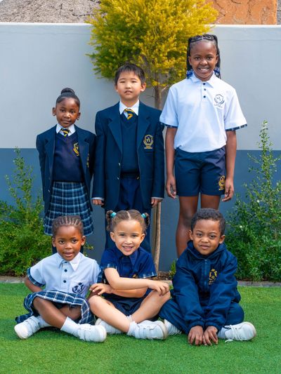 Group of six school children in diverse Aquila Montessori uniforms posing outdoors on grass.
