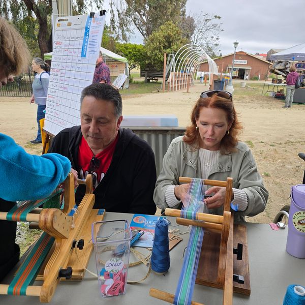 Two people weaving fabric at a craft fair.