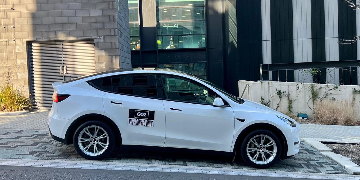 White Tesla Model Y parked with a "PRE-BOOKED ONLY" sign on the door.