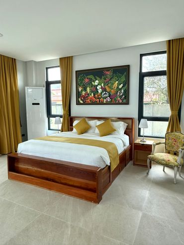 Modern bedroom with wooden bed, mustard curtains, and floral painting.