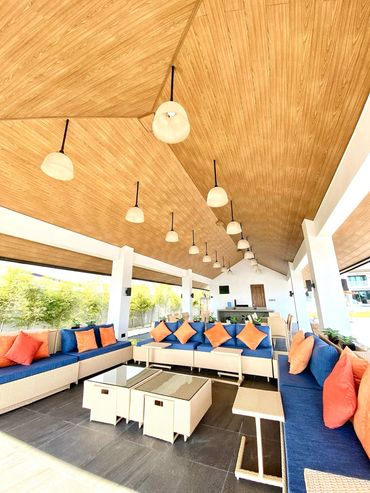 Spacious outdoor lounge with blue sofas and orange cushions under a wooden ceiling.