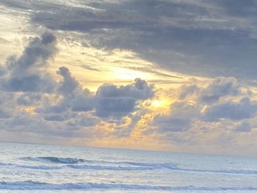 Sunset over calm ocean waves with dramatic cloud formations.