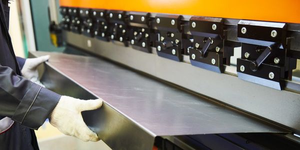 Worker handling a large metal sheet with industrial machine.