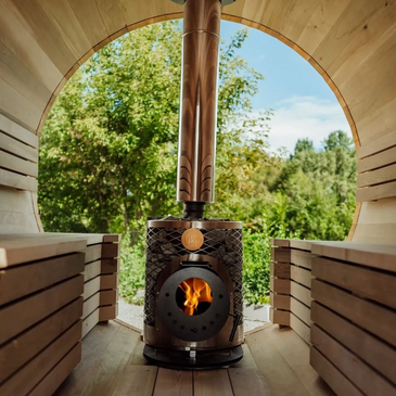 Wood-fired stove inside a wooden cabin with a view of green trees.