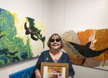 Lynda holding the framed Costco Connection article at ECCO gallery