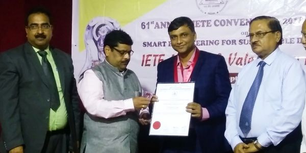 A man receives an award certificate from another man at a formal event with others standing beside them.