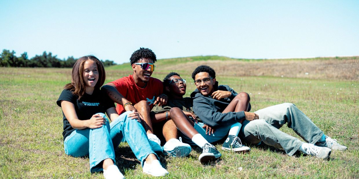 A group of teenagers sitting on the grass hanging out and laughing