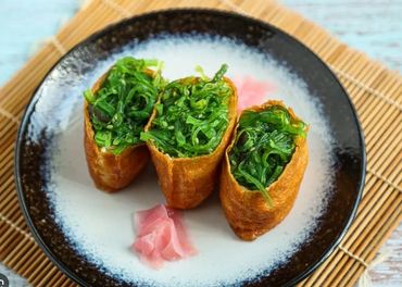 Three seaweed-filled inari sushi pieces with pickled ginger on a black and white plate.