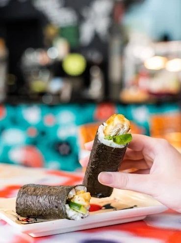 Hand holding sushi hand roll with another on a plate.