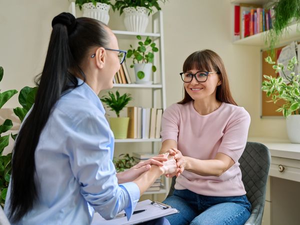 Two women, both wearing glasses, are sitting and holding hands, smiling at each other.