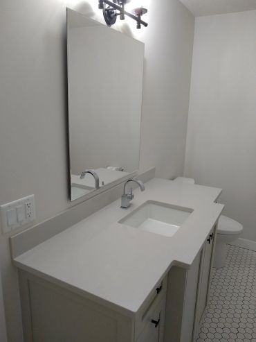 Modern white bathroom vanity with a rectangular mirror and hexagonal tile floor.