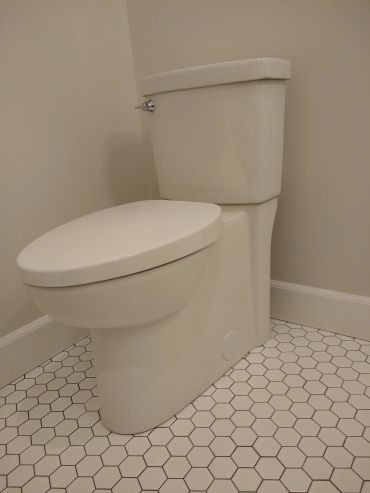 A clean white toilet against a beige wall with hexagonal tile flooring.