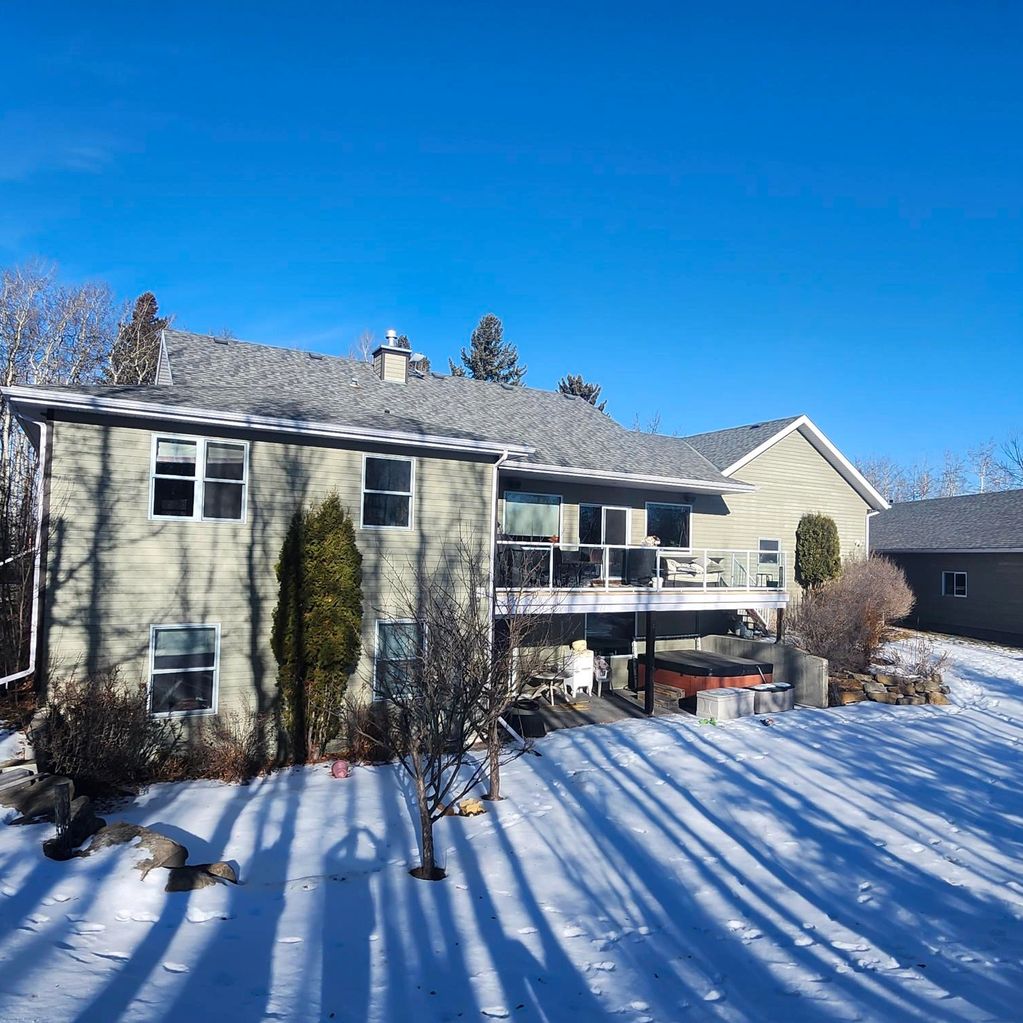 A snowy backyard with a modern house and long tree shadows under a clear blue sky.